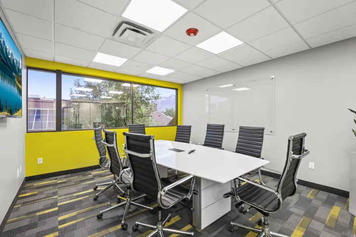 Window-lined room featuring a large mounted display, modular ceiling tiles with integrated lighting, and patterned carpet