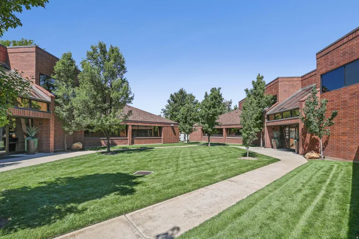 Brick exterior building with expansive lawn, mature trees, concrete pathways, and architectural glass features