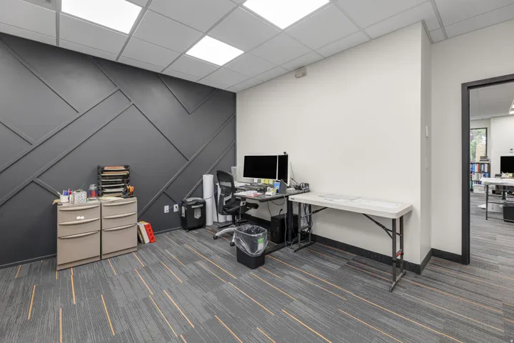 Accent wall with geometric paneling, dropped ceiling with integrated lighting, and carpet flooring with linear accents