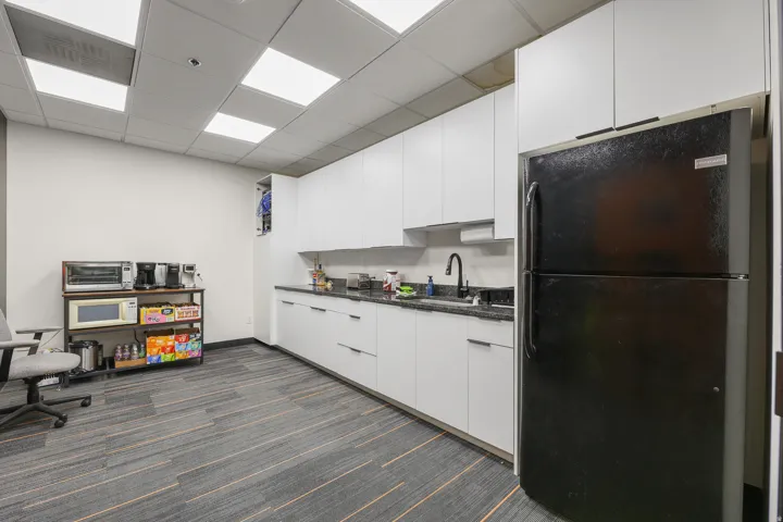 Kitchenette with white flat-panel cabinetry, dark speckled countertops, and a black refrigerator