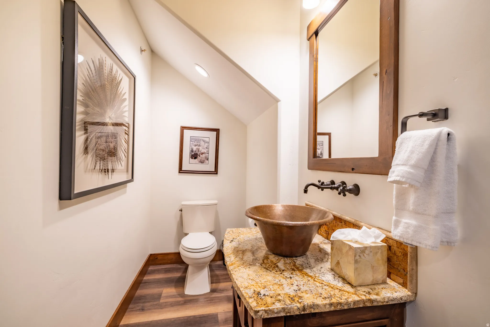 Granite countertop with a copper vessel sink, wood-finish flooring, and a natural wood-framed mirror