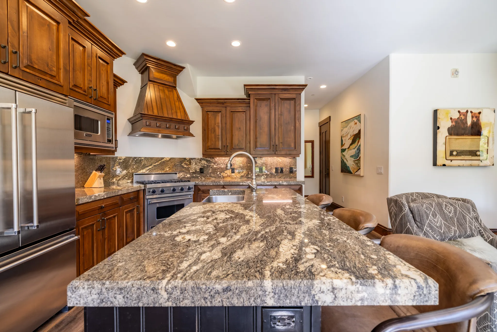 Kitchen featuring rich wood cabinetry, stainless steel appliances, a large island with a natural stone countertop, and recessed lighting