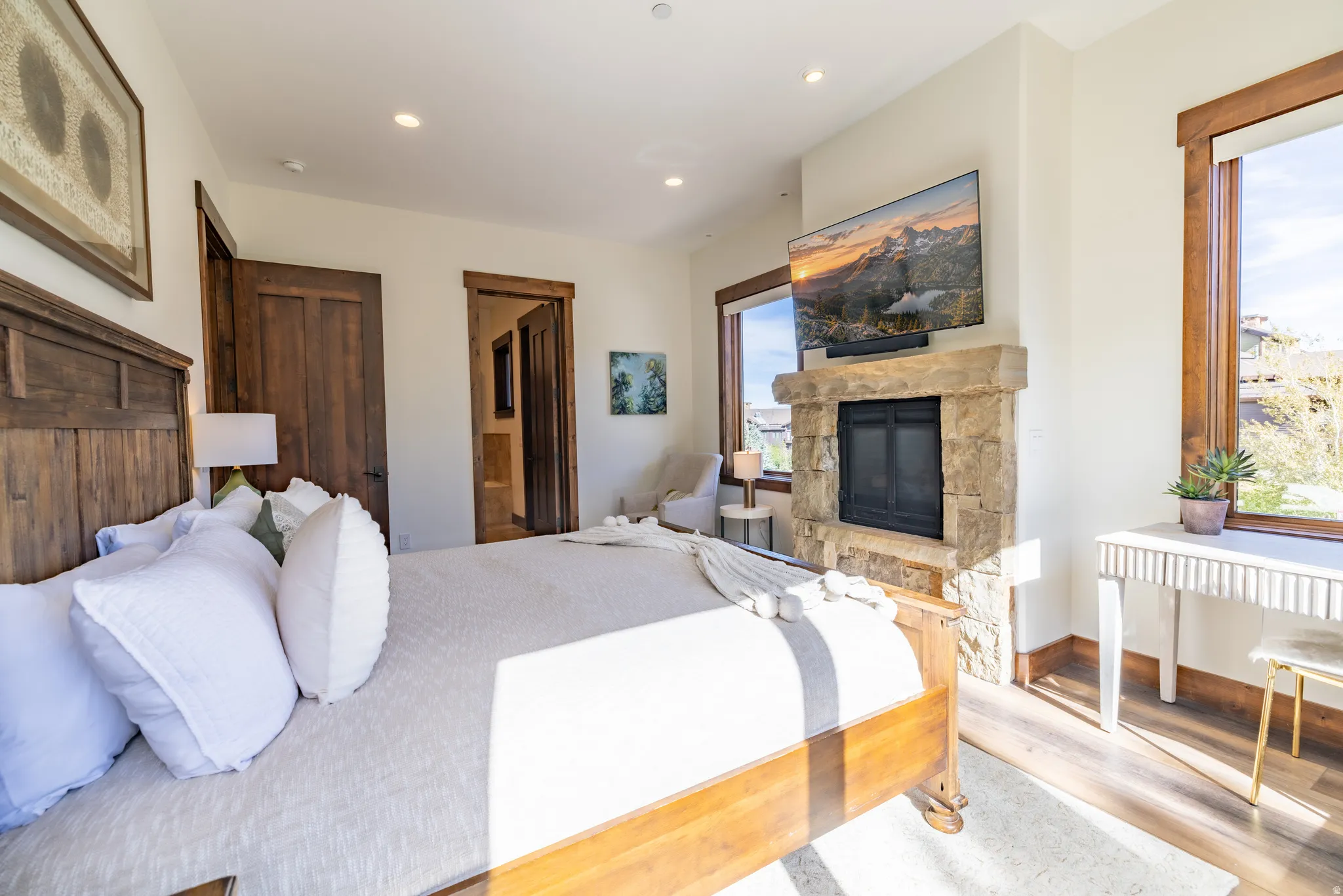 Stone-clad fireplace with a dark metal firebox, wood-finish flooring, recessed lighting, and wood-trimmed windows