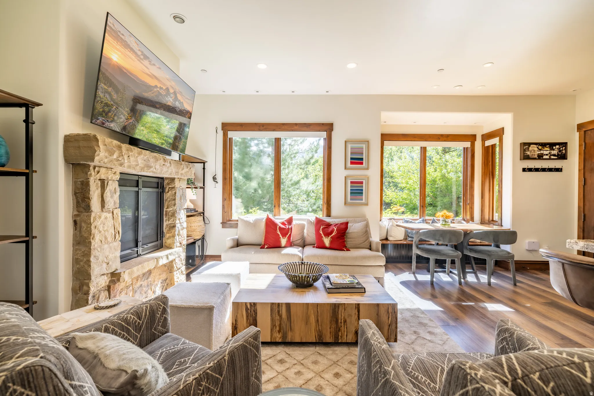 Stone-clad fireplace with a hearth, wood-finish flooring, recessed lighting, built-in dining nook with bench seating, and wood-framed windows