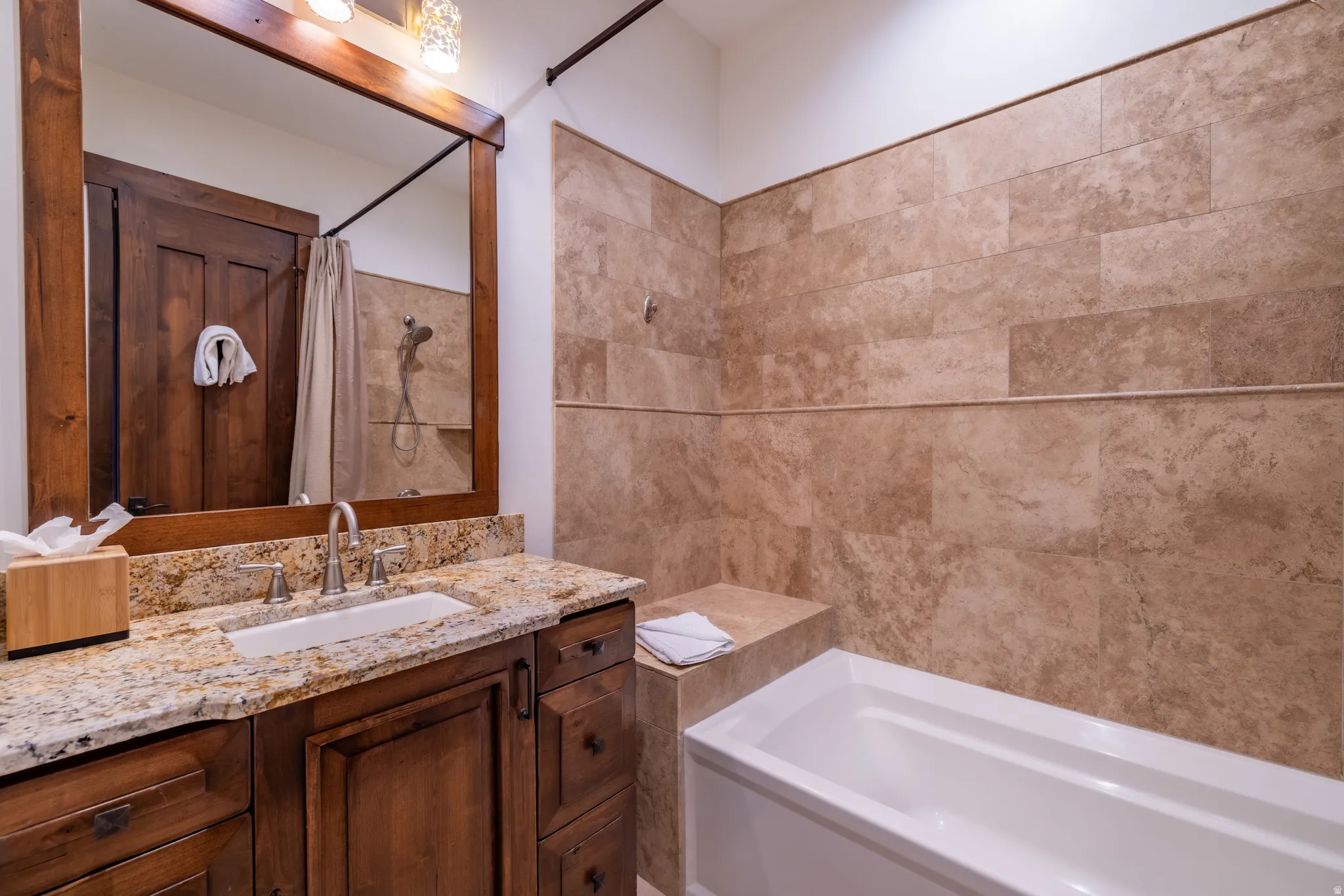 Wood-finish vanity with an undermount sink, stone countertop, and large framed mirror