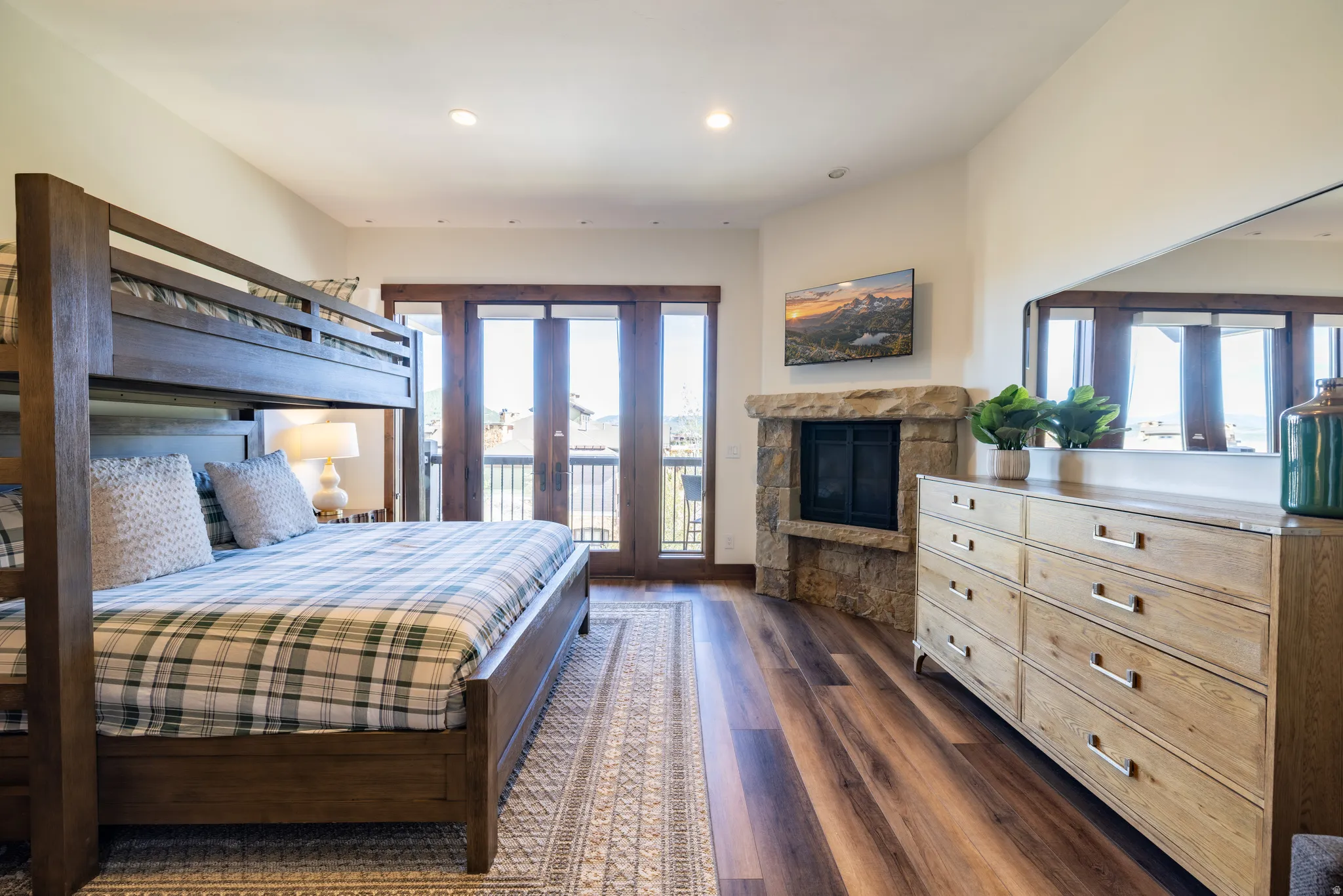 Stone-clad fireplace, wood-finish flooring, recessed lighting, and French doors opening to a balcony