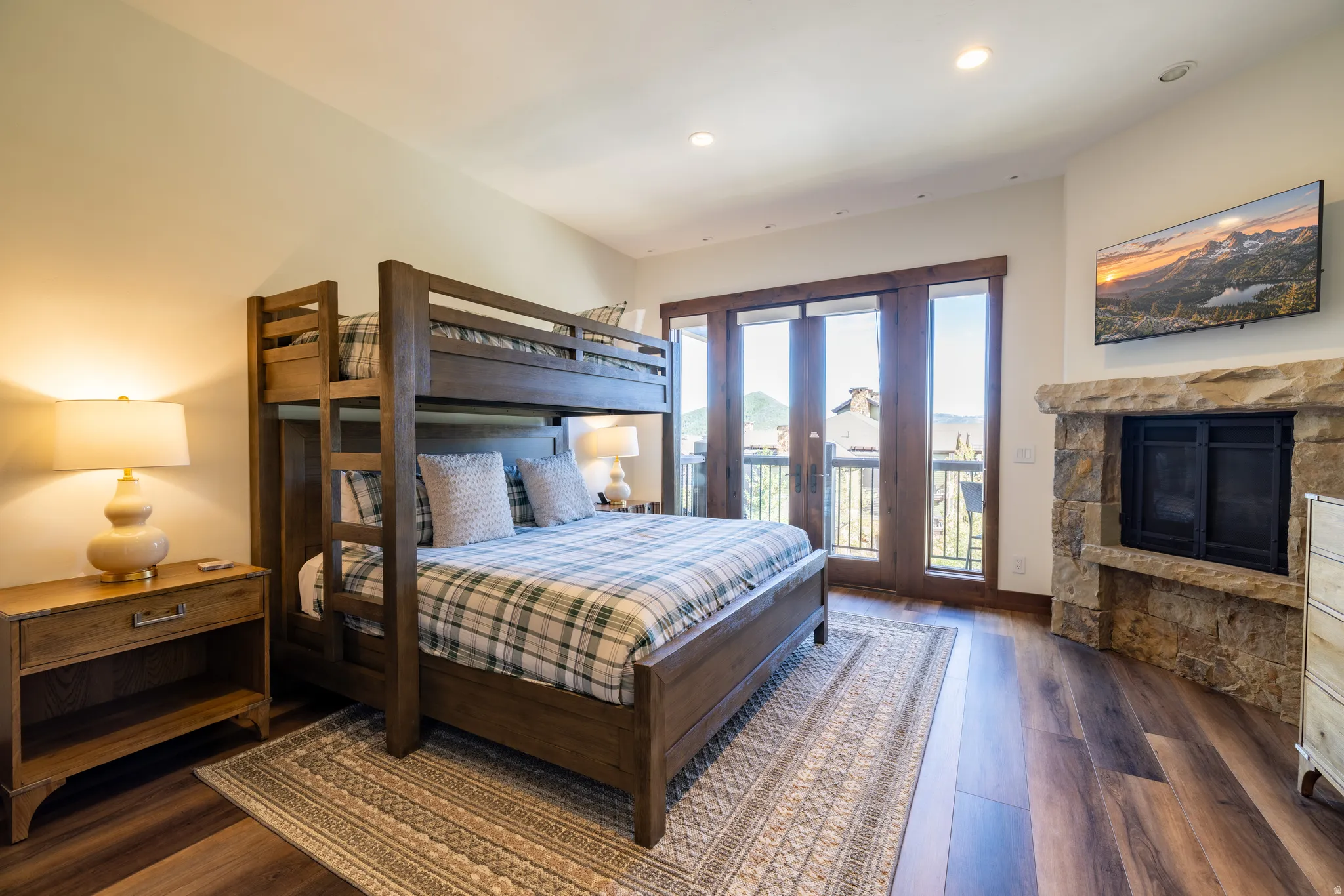 Wood-finish flooring, stone-clad fireplace, built-in shelving, wood-framed glass doors, and recessed lighting