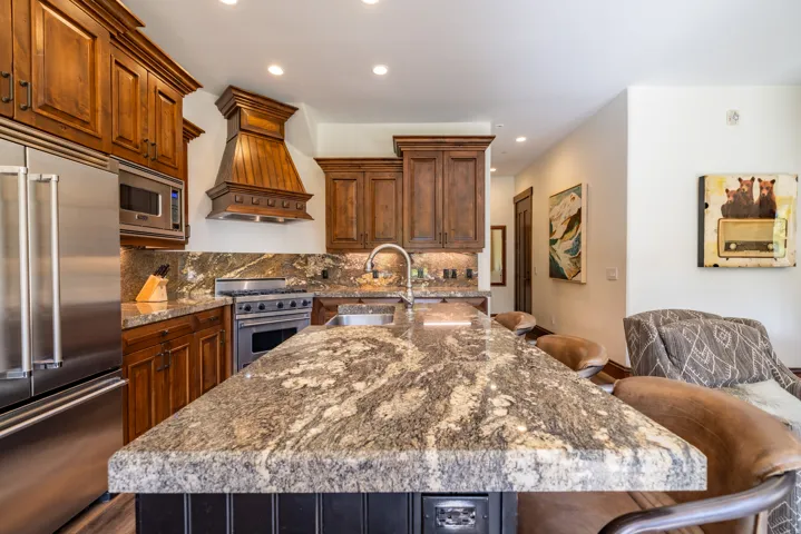 Kitchen featuring rich wood cabinetry, stainless steel appliances, a large island with a natural stone countertop, and recessed lighting