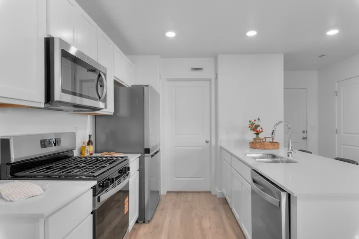 Modern kitchen featuring stainless steel appliances, white cabinetry, light countertops, a kitchen island, and wood-finish flooring