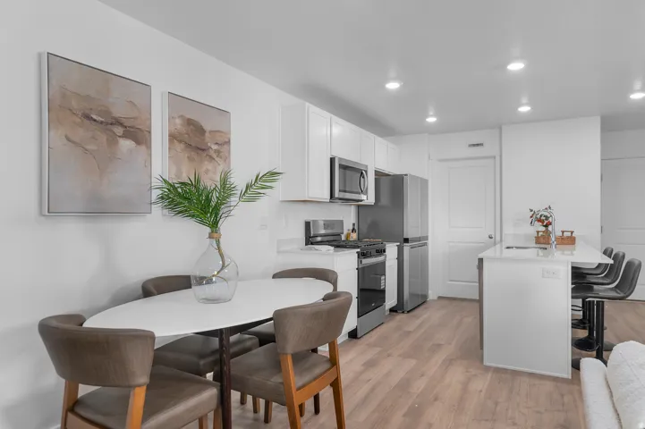 White cabinetry, stainless steel appliances, recessed ceiling lights, wood-finish flooring, and a kitchen island with seating
