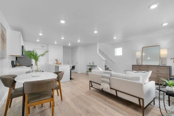 Open-concept living space featuring wood-finish flooring, recessed lighting, white cabinetry, and a kitchen island with seating