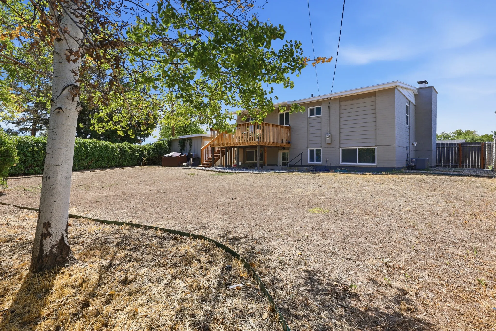 Expansive outdoor area featuring a wood deck, built-in stairs, mature trees, and a privacy hedge