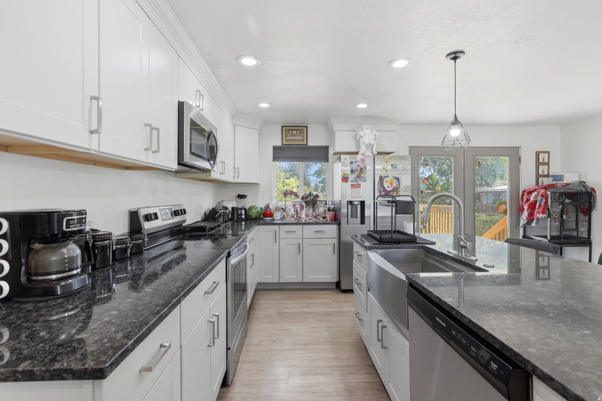 Kitchen featuring white cabinetry, dark stone countertops, stainless steel appliances, and wood-finish flooring