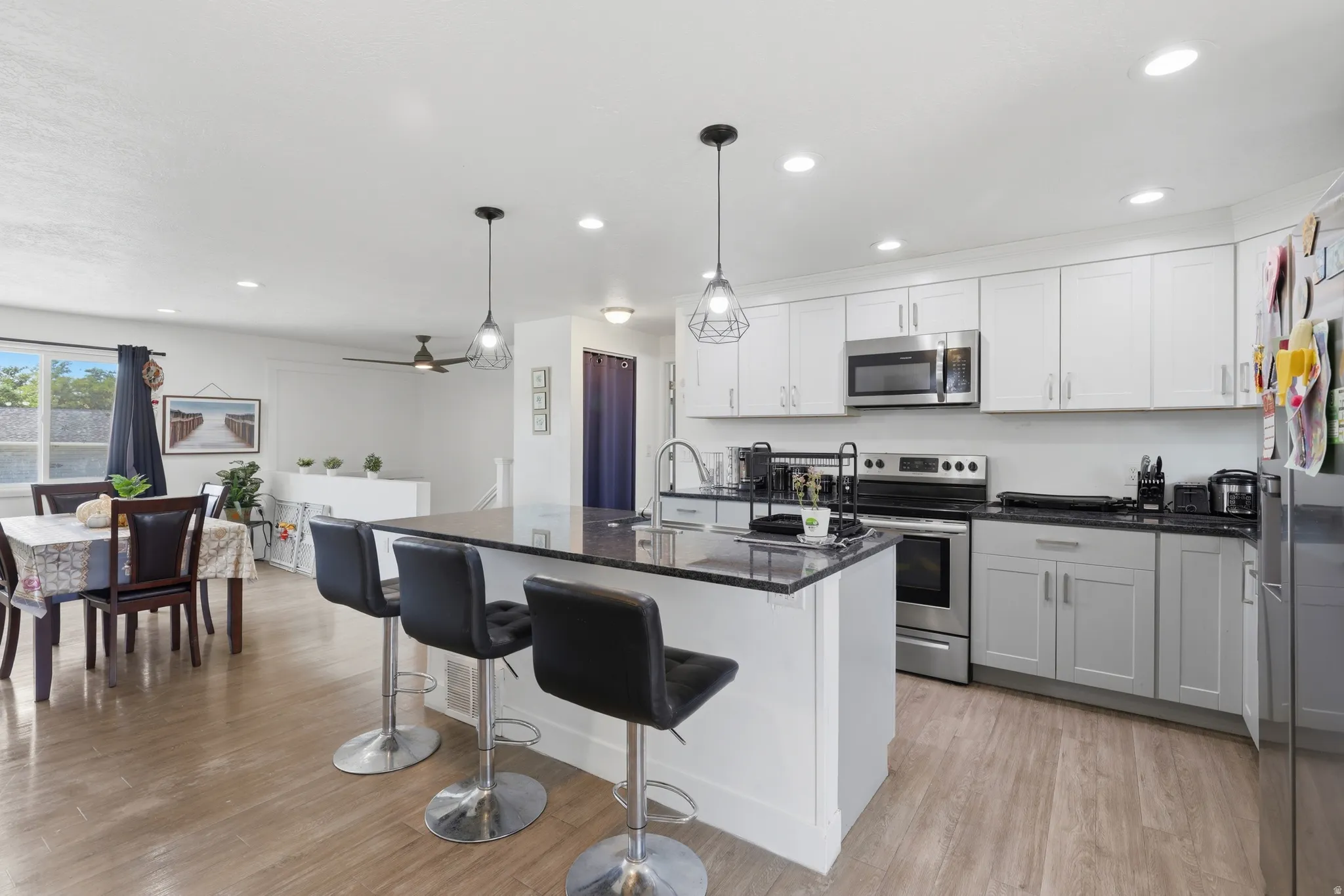 Kitchen featuring an island with seating, stainless steel appliances, dark countertops, white upper cabinetry, and light gray lower cabinetry