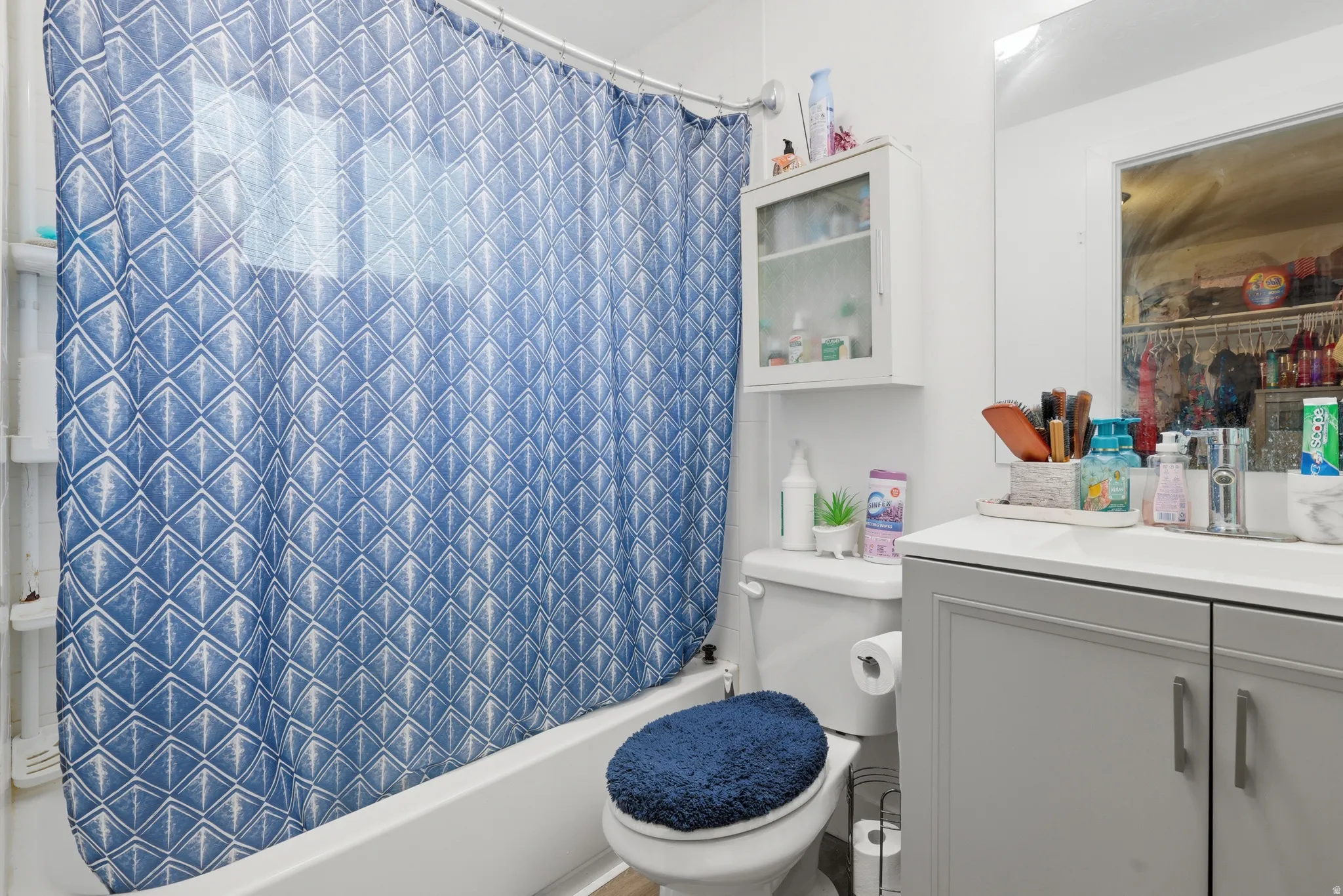 White bathtub with a curved shower rod, built-in wall shelving, light gray vanity with dual cabinet doors, and a wall-mounted medicine cabinet