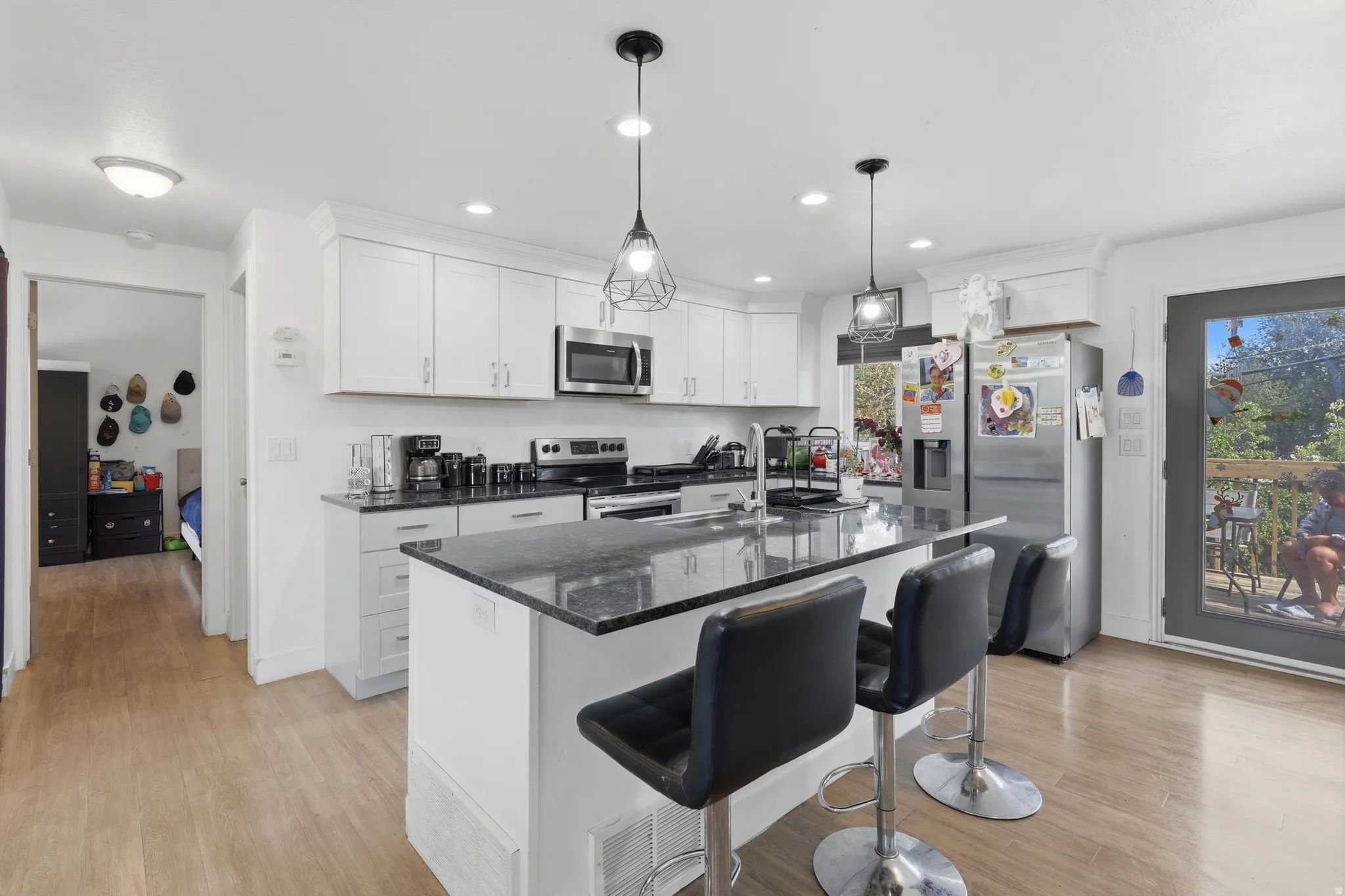 Kitchen featuring white cabinetry, dark countertops, stainless steel appliances, a center island with seating, and wood-finish flooring