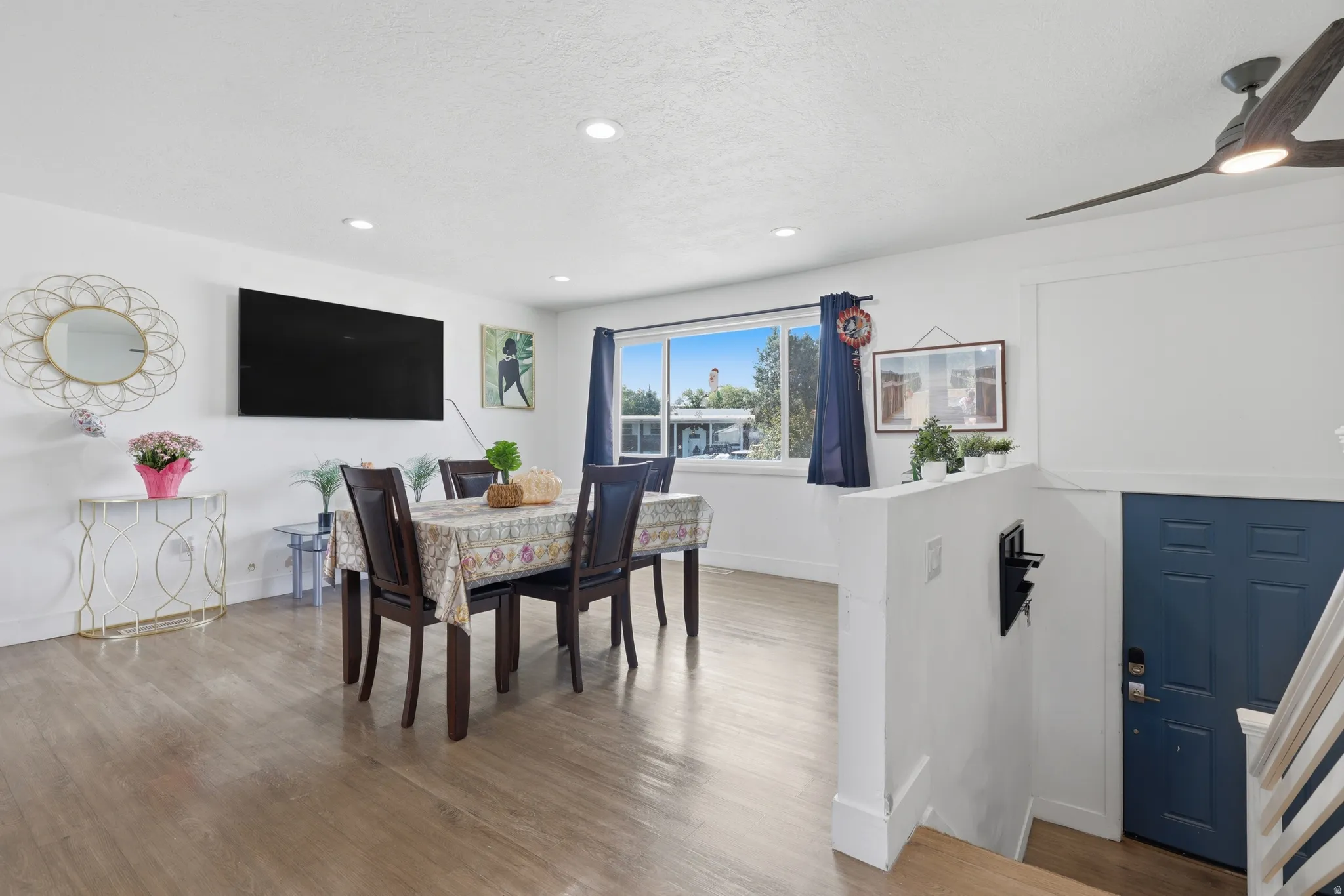 Recessed ceiling lighting, wood-finish flooring, white painted walls, a dark blue entry door, and a ceiling fan with integrated lighting