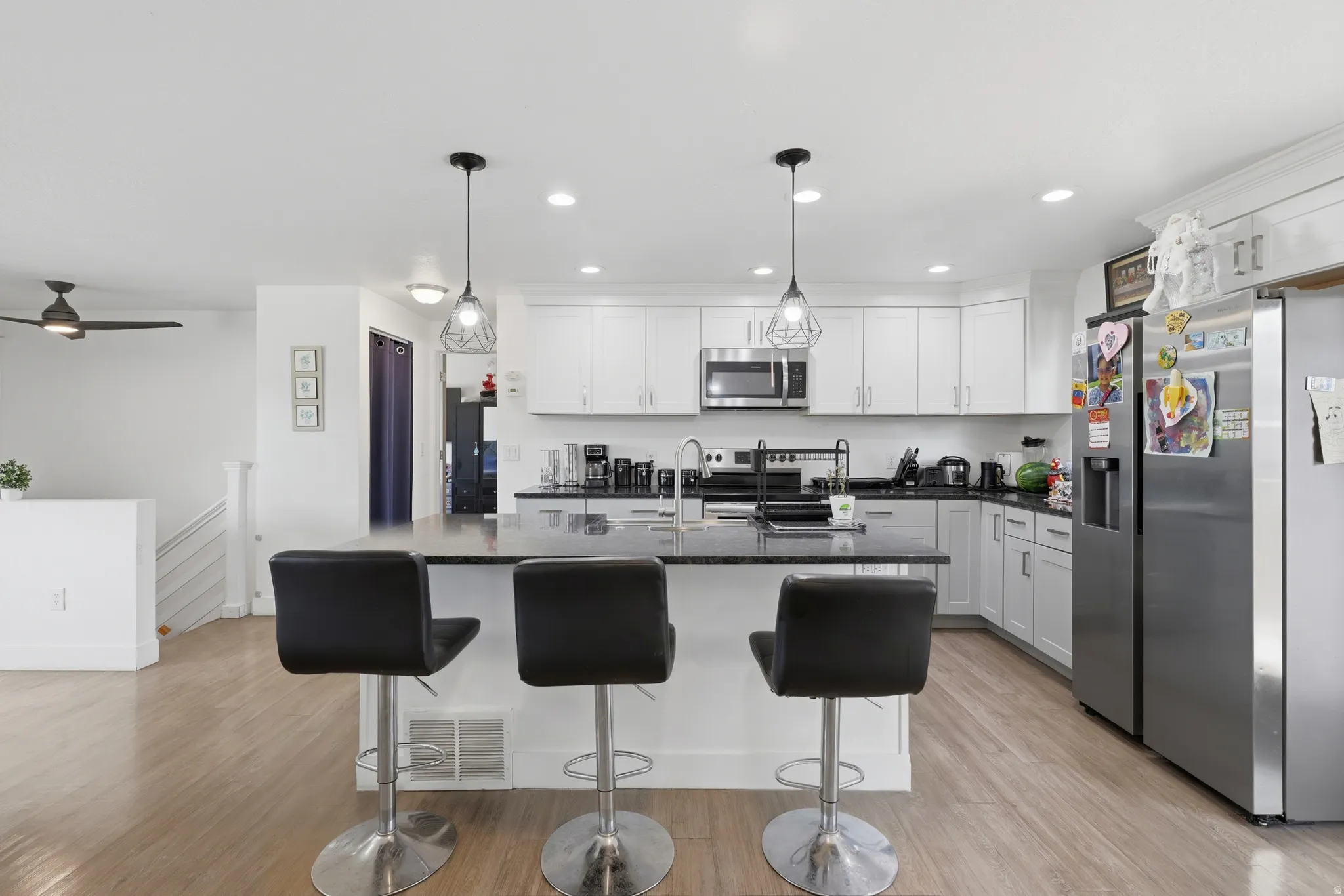 Kitchen featuring white cabinetry, stainless steel appliances, a center island with seating, dark countertops, and wood-finish flooring