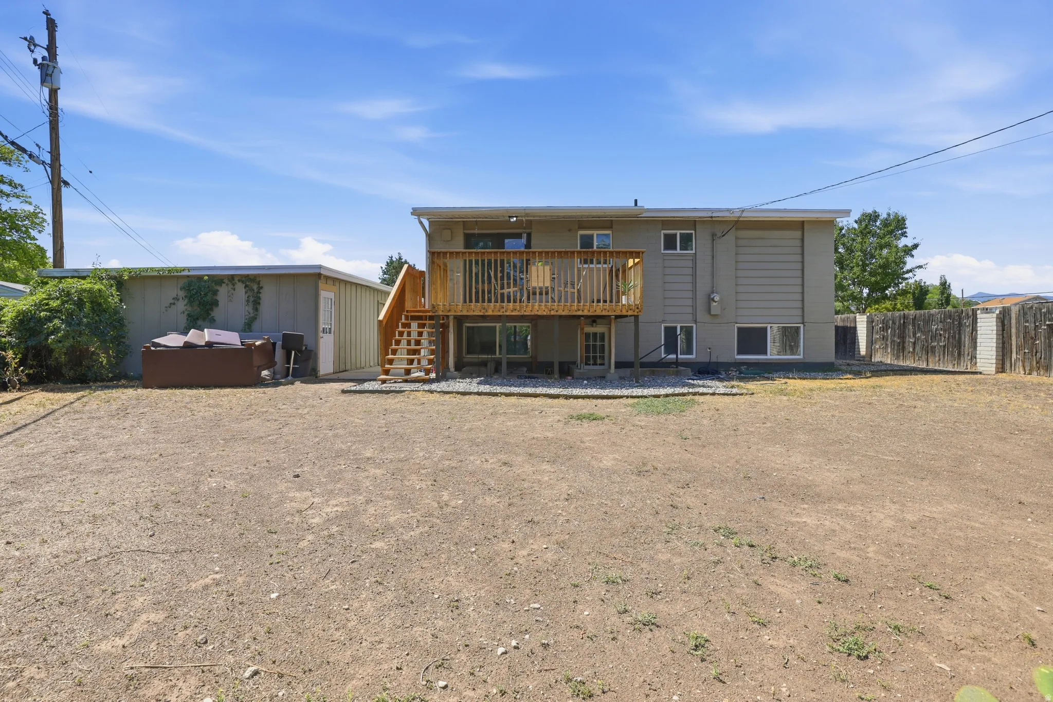 Expansive rear yard with a wood deck, exterior staircase, and detached storage shed