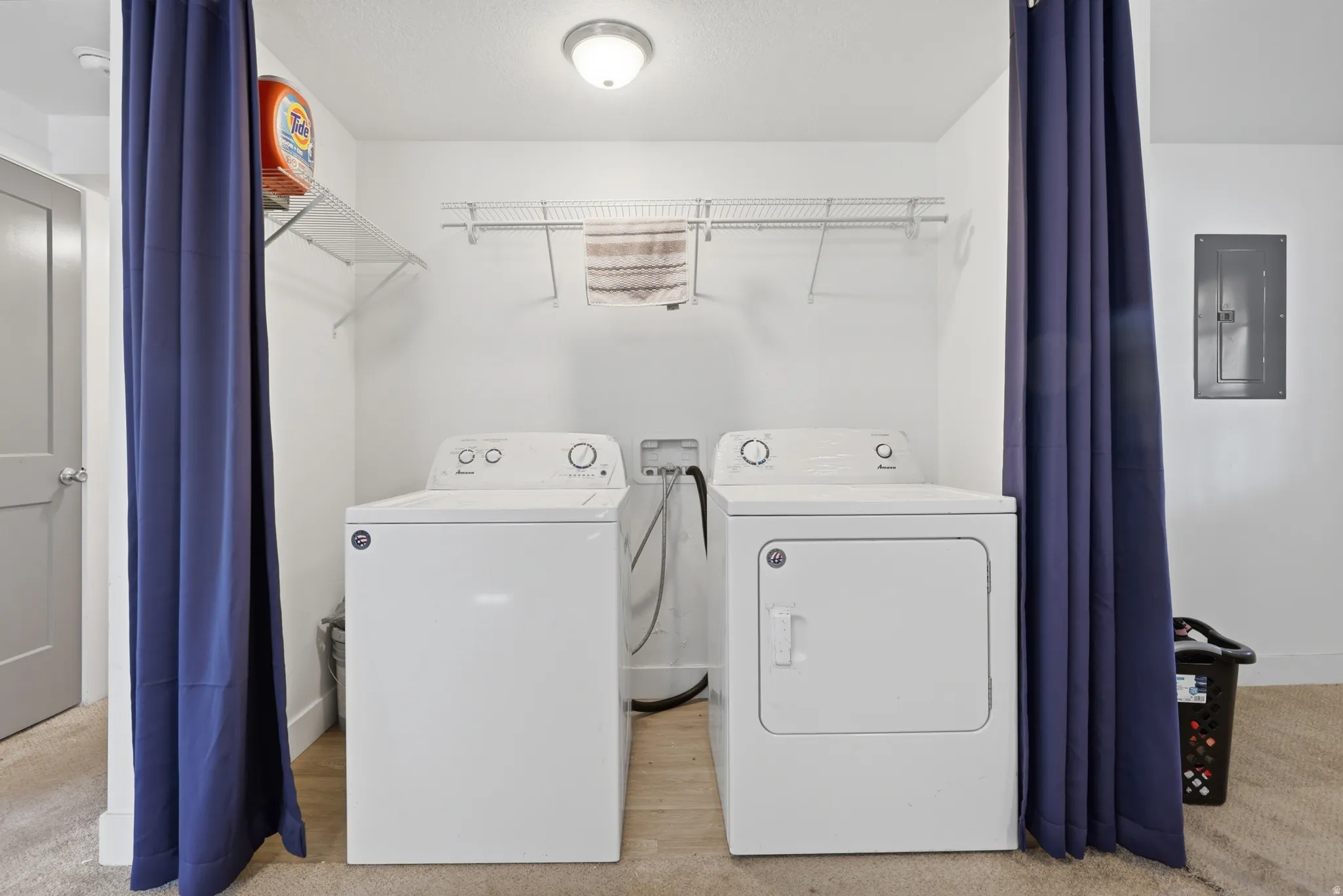 Dedicated laundry area featuring a washer and dryer, convenient overhead wire shelving, and wood-finish flooring