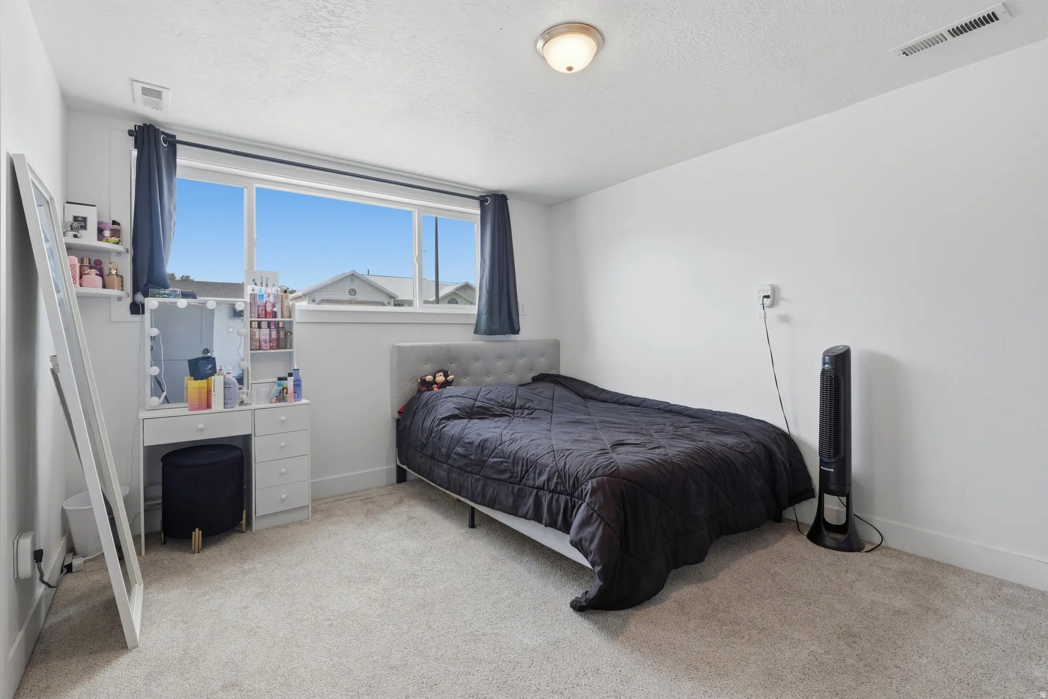 Light-toned carpeting, ample natural light from a large window, a built-in floating shelf, and a ceiling-mounted light fixture