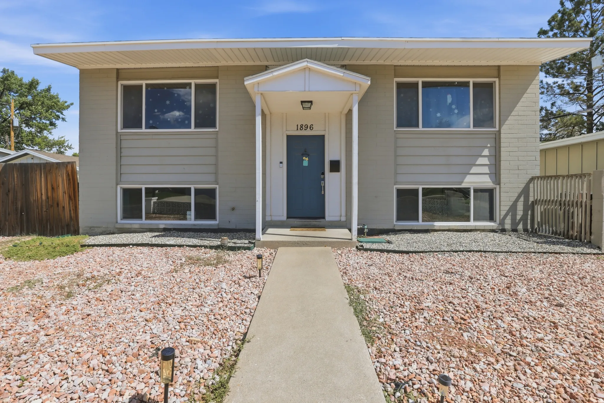 Split-level exterior with a portico entry, a blue front door, white window frames, and a low-maintenance gravel front yard