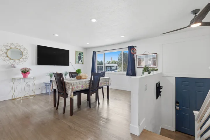 Recessed ceiling lighting, wood-finish flooring, white painted walls, a dark blue entry door, and a ceiling fan with integrated lighting