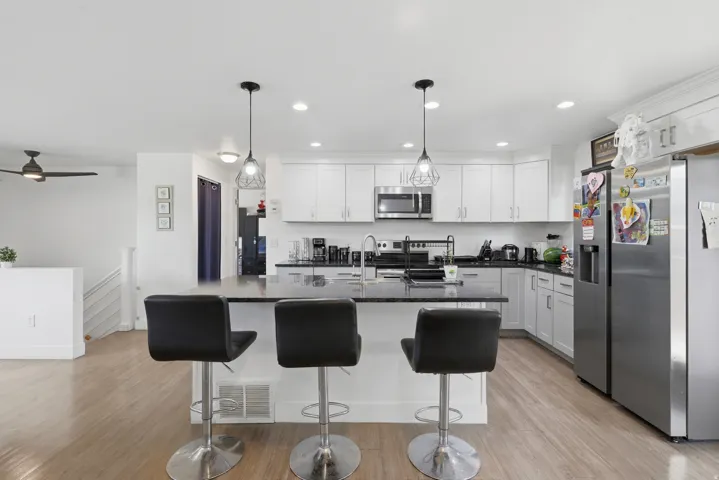 Kitchen featuring white cabinetry, stainless steel appliances, a center island with seating, dark countertops, and wood-finish flooring