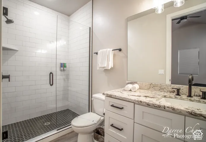 Bathroom featuring a glass-enclosed shower with white subway tile, dark hexagonal floor tile, stone-finish countertop, white vanity cabinet with matte black hardware, and an expansive wall-mounted mirror
