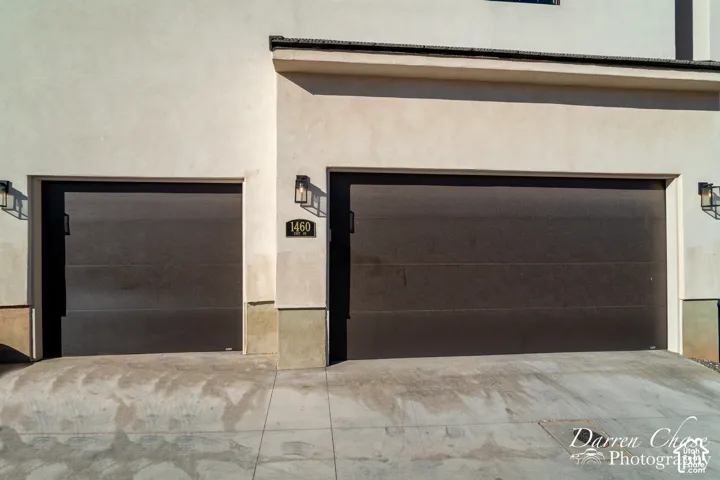 Stucco exterior featuring a three-car tandem garage with dark horizontal-panel doors and wall-mounted exterior light fixtures
