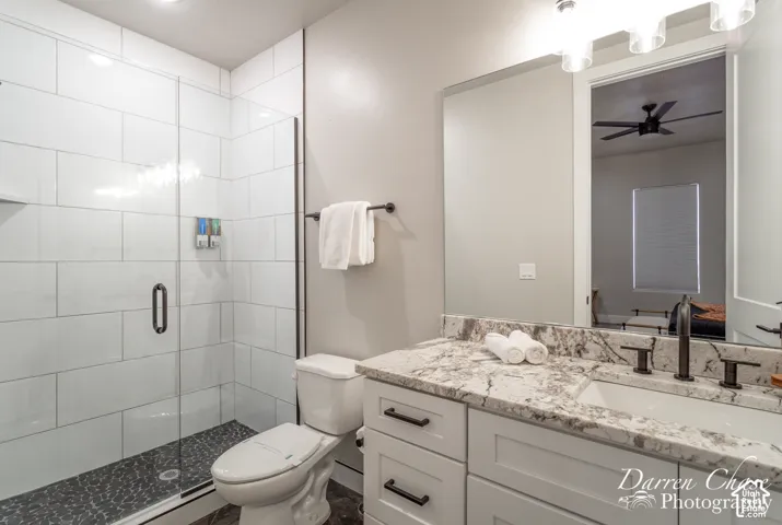 Bathroom featuring a white subway tile walk-in shower with a glass door, patterned stone countertop, shaker-style vanity cabinetry, matte black hardware, and an oversized wall-mounted mirror