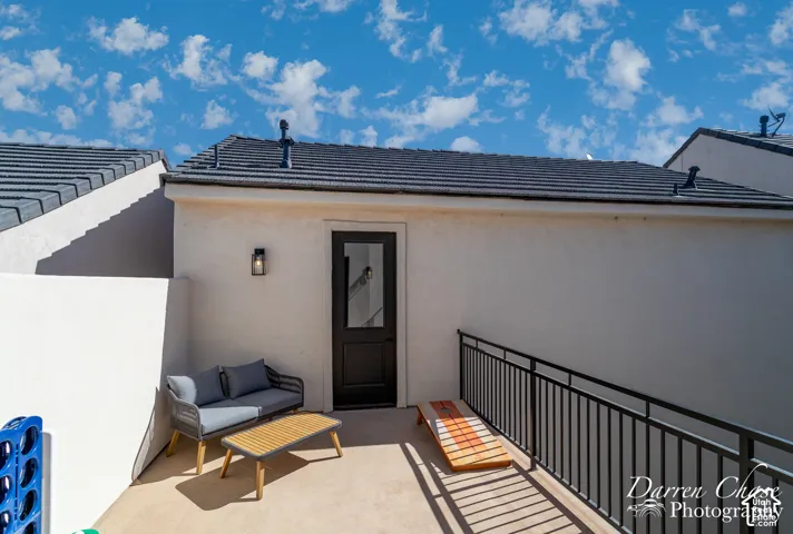 Exterior deck with light-toned concrete flooring, dark metal railing, a single-lite glass entry door, and wall-mounted exterior light fixture