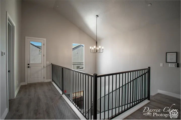 Vaulted ceilings, wood-finish flooring, metal spindle railing, and a multi-arm chandelier
