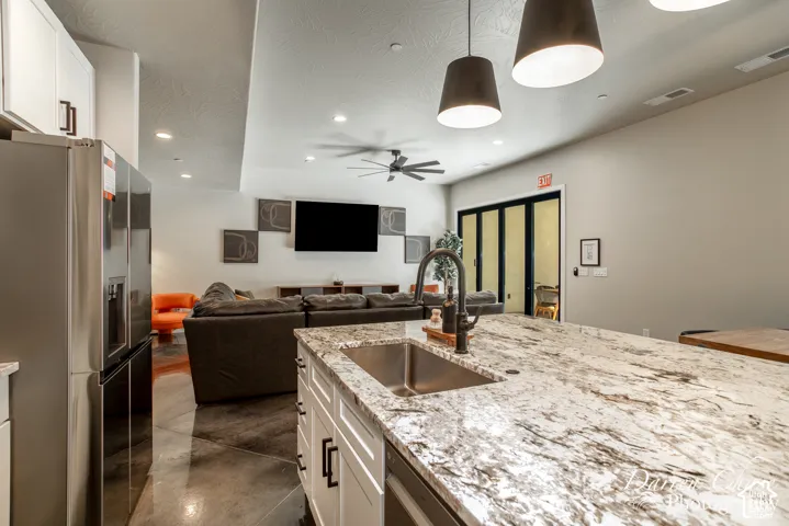 Kitchen island featuring a stone-look countertop, undermount stainless steel sink, and dark hardware, complemented by white cabinetry, pendant lighting, and polished concrete flooring