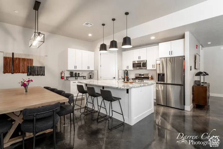 Kitchen featuring white shaker-style cabinetry, stone-surface countertops, central island with breakfast bar seating, stainless steel appliances, and polished concrete flooring