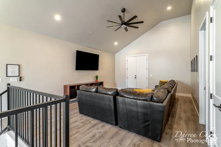 Vaulted ceilings featuring recessed lighting, a multi-blade ceiling fan, wood-finish flooring, and a black metal handrail