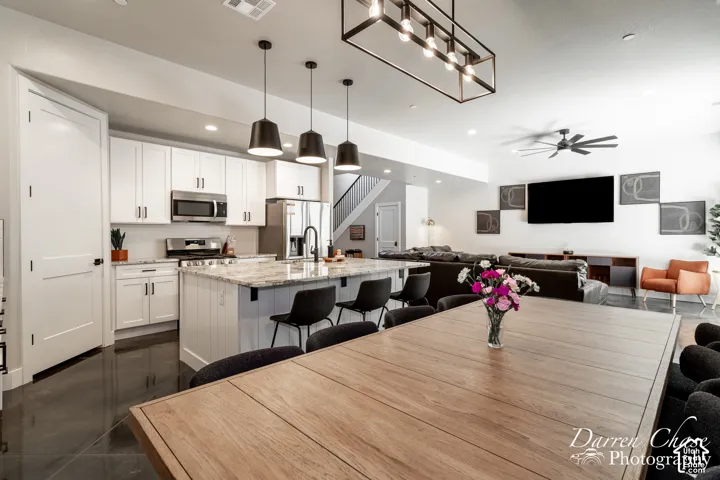Kitchen featuring white shaker cabinetry, stone-surface island, stainless steel appliances, tiered pendant lighting, and dark reflective flooring