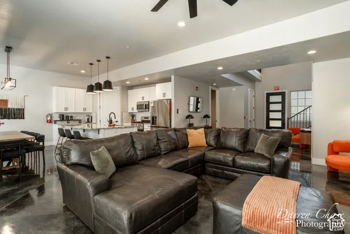 Open-concept interior featuring polished concrete flooring, white shaker-style cabinetry, stainless steel appliances, tiered pendant lighting, and a multi-pane glass entry door