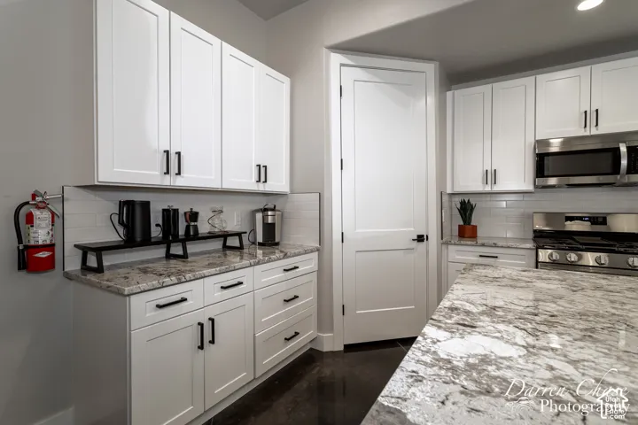 Kitchen featuring white shaker-style cabinetry, patterned stone countertops, stainless steel appliances, and subway tile backsplash