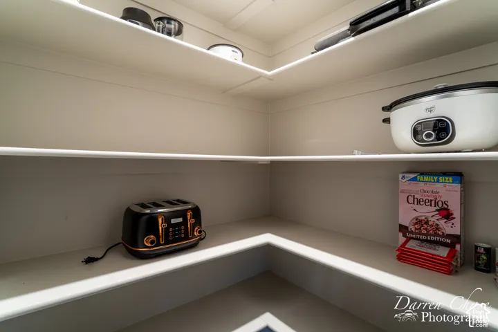 Walk-in storage space featuring multi-level, corner-wrapped shelving with a crisp, neutral finish