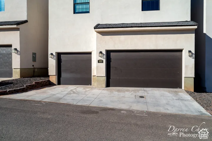 Stucco exterior featuring a three-car garage configuration, dark-finish sectional doors, and exterior wall-mounted lighting