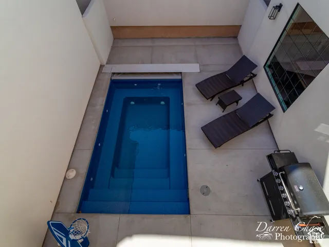 Private courtyard featuring a rectangular in-ground pool with built-in stairs, smooth concrete patio, and wall-mounted exterior lighting