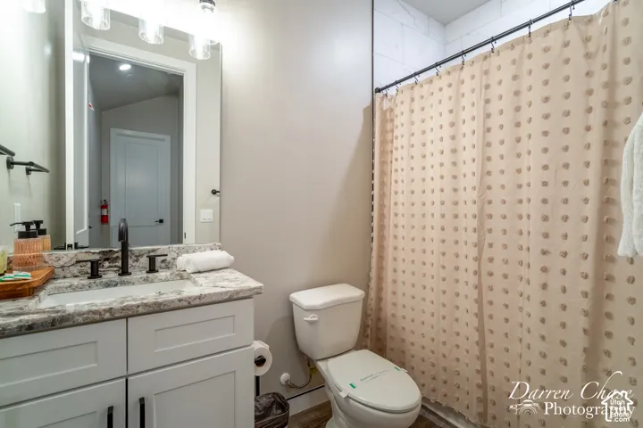 Bathroom featuring a white shaker-style vanity cabinet, stone-finish countertop with an integrated rectangular sink, matte black widespread faucet, and full-width vanity mirror with integrated multi-bulb light fixture