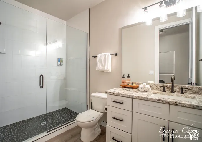 Walk-in shower with floor-to-ceiling white tile and stone-texture floor, vanity with stone countertop, undermount sink, and matte black fixtures