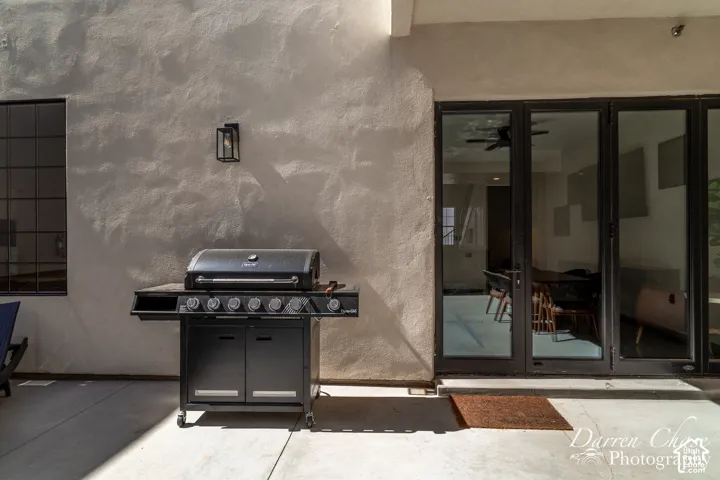 Exterior patio featuring a textured stucco wall, multi-panel glass door system with dark frames, and a wall-mounted exterior lantern light