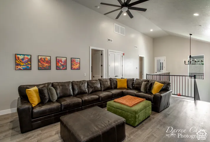 Vaulted ceilings, wood-finish flooring, matte black ceiling fan, and black metal stair railing
