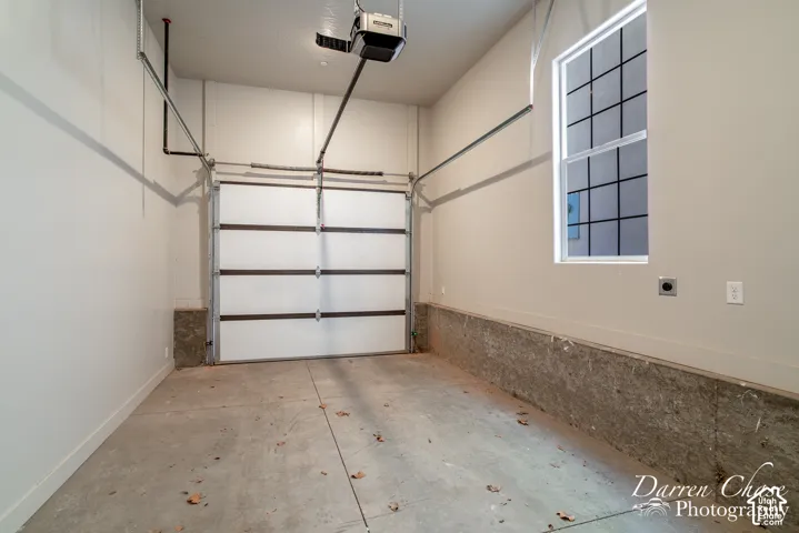 Garage interior featuring a concrete floor, high ceilings with an automatic door opener, a vertical window with pane detailing, and concrete foundation walls