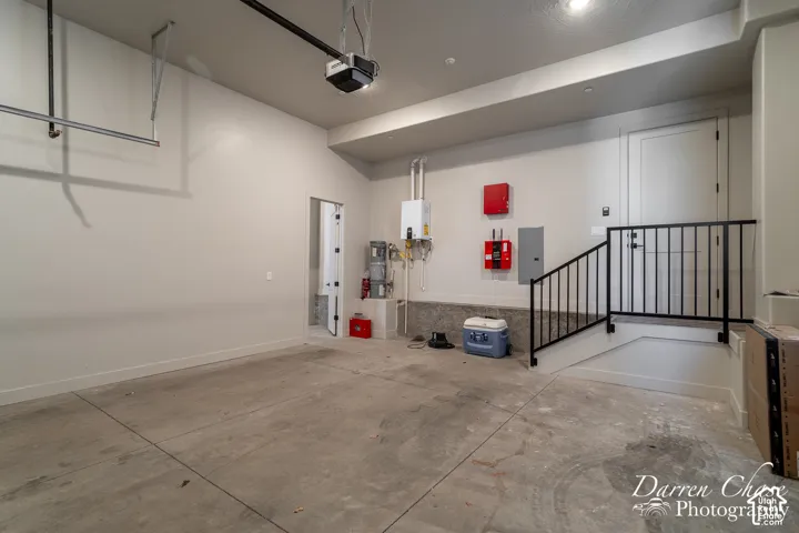 Finished garage interior featuring smooth-finish concrete flooring, high ceilings with mounted door opener, wall-mounted tankless water heater, and metal handrail with vertical balusters