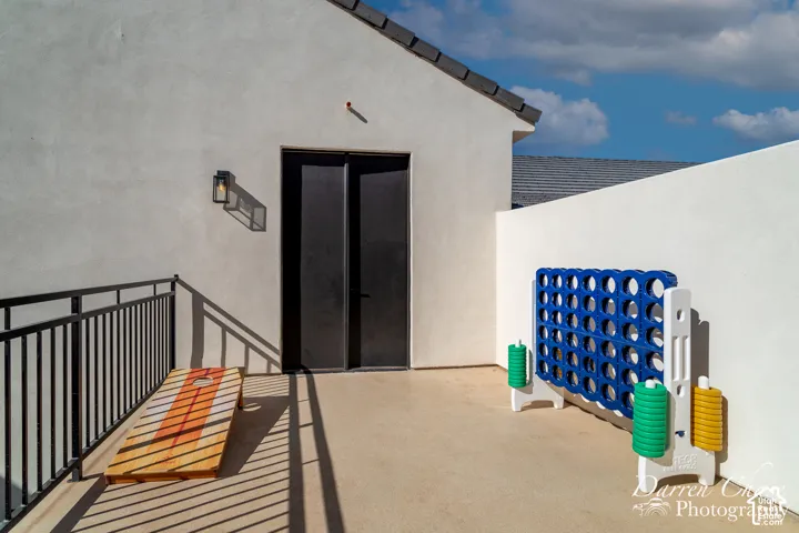 Exterior balcony featuring smooth stucco walls, concrete flooring, dark metal double-door entry, black railing, and wall-mounted exterior lighting