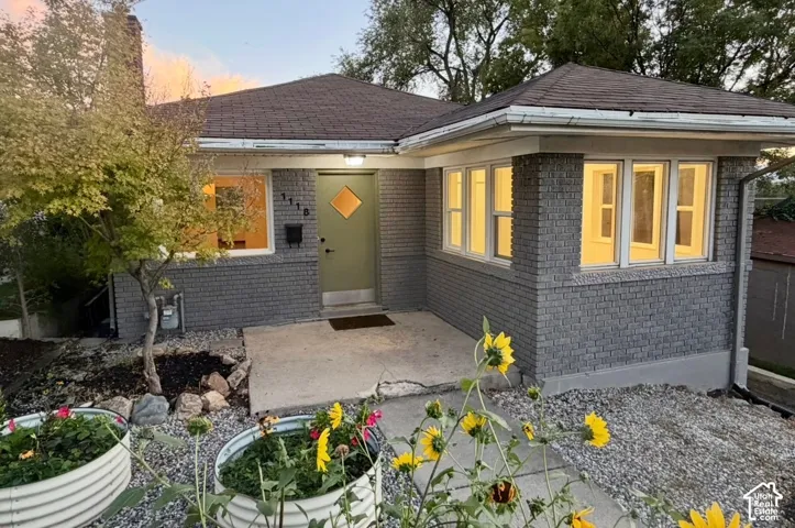 Gray brick exterior with a gray-green front door, white trim windows, and a dark shingle roof